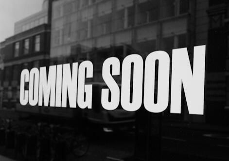 A black-and-white image of a sign on a building exterior that reads COMING SOON.